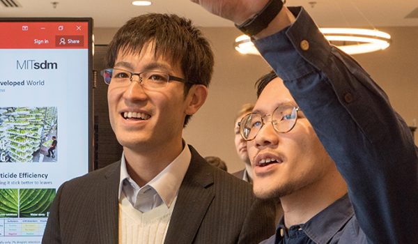 Two students look at a poster, one raising his arm to point at a part of it.