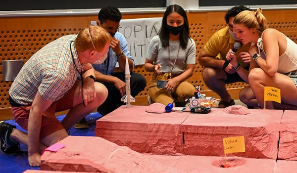 Students gather around a Lego rover, which is navigating a model of the Martian landscape