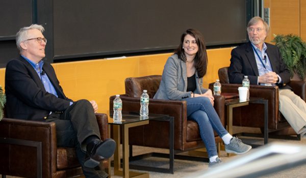 Three adults sit in leather armchairs facing an audience. They are all smiling.