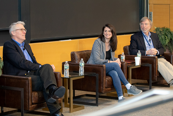 Three adults sit in leather armchairs facing an audience. They are all smiling.