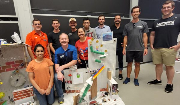 A group of students gather around a complicated homemade Rube Goldberg device.