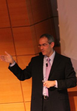 Steve Eppinger, a man in a black suit and a pink tie, in the middle of delivering a talk