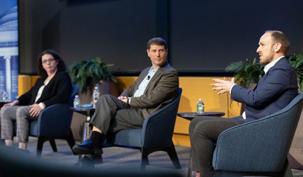 Megan Mitchell and J. Robert Wirthlin watch as Robert Plummer gestures while speaking.