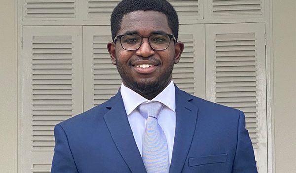 Headshot of Evans Adusei, an African man wearing a navy suit and glasses. He's smiling at the camera.