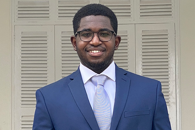 Headshot of Evans Adusei, an African man wearing a navy suit and glasses. He's smiling at the camera.