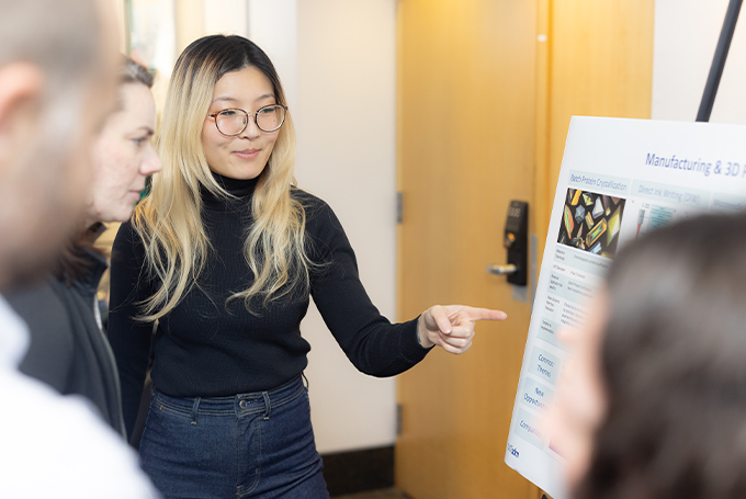 A student points at a poster on an easel with others pointing at it.